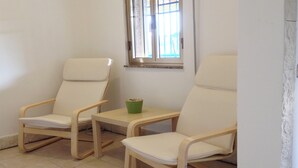 Deux chaises en bois avec des coussins blancs, une petite table et une fenêtre avec des barreaux.
