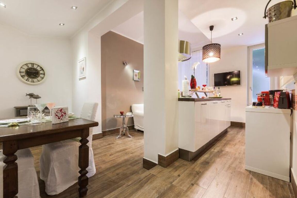 Une cuisine moderne avec des meubles blancs, un coin repas doté d’une table en bois, et un espace de vie comprenant un canapé et une petite table d’appoint.