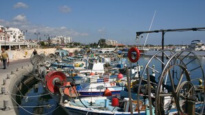Un puerto deportivo con barcos amarrados, una rueda hidráulica y edificios al fondo.