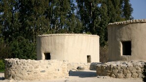 Un sitio histórico con antiguas construcciones de piedra, incluyendo una estructura circular y un edificio rectangular con una ventana.