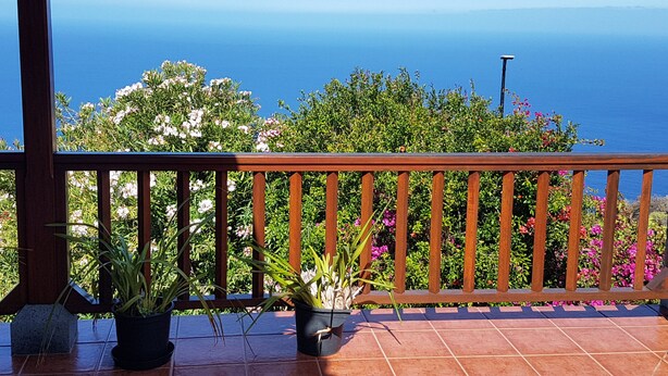 A balcony with a wooden railing overlooking a scenic view of the sea.