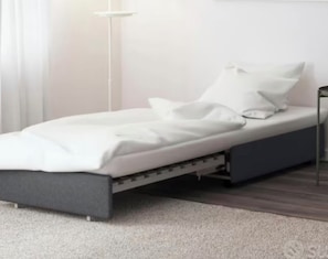 A single bed with a grey frame, white bedding, and a bedside table with a lamp.