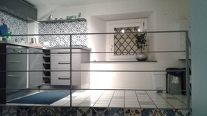 A kitchen with patterned tiles, a sink, cabinets, and a window with a plant. - The ancient alley, just a step away from everything (Salerno)