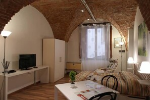 A cozy room with a brick ceiling, a bed with striped bedding, a desk with a TV, and a small plant. - LE VOLTE - Romantic studio in the historical center with AC&Wifi (Lucca)