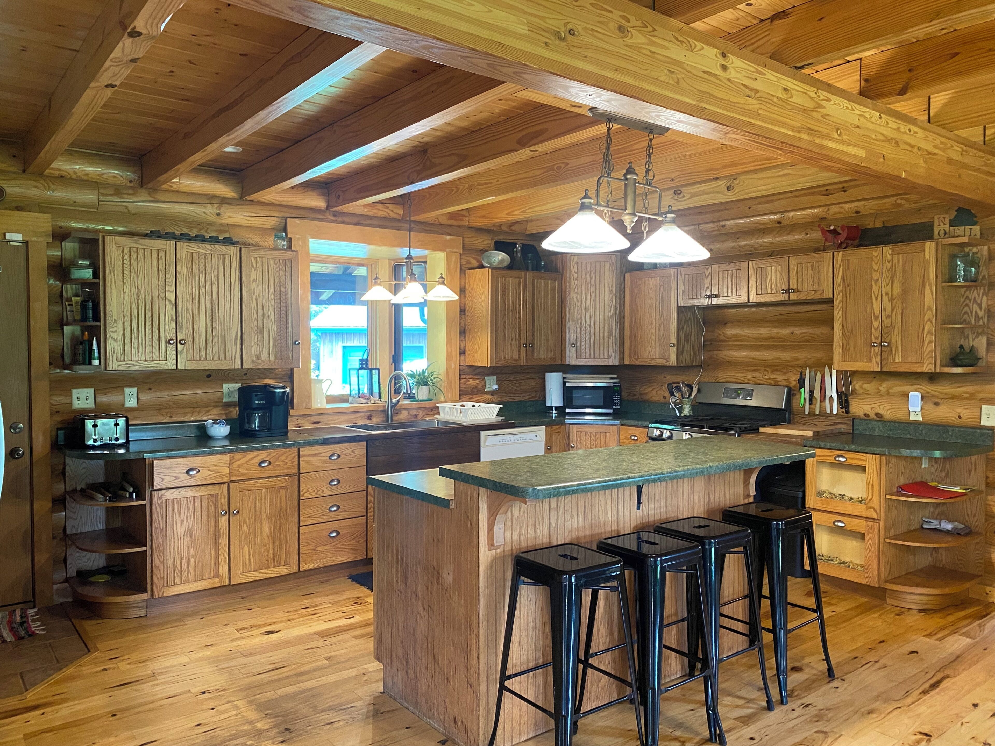 L’intérieur d’un chalet en bois comprend un coin cuisine, des placards en bois, des tabourets de bar et une grande fenêtre.