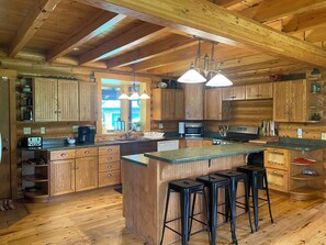 A wooden cabin interior with a kitchen area, wooden cabinets, a bar stool seating, and a large window. - Lodge on Pine Ridge, with private 50 acres (Emlenton)