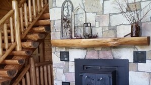 A log cabin interior with a stone fireplace, wooden staircase, and a patterned sofa. - Lodge on Pine Ridge, with private 50 acres (Emlenton)