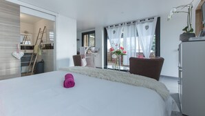 Ein modernes Hotelzimmer mit einem großen Bett, Blick ins Freie, einer Essecke und einem Balkon mit Blumen.