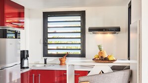 Eine moderne Küche mit roten Schränken, einer Kaffeemaschine, einer Obstschale und einem Fenster mit Jalousien.