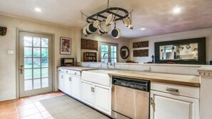 A kitchen with white cabinets, a dishwasher, and a hanging pot rack. - Dallas Love Field Bluffview Bluebonnet Road Bungalow (Dallas)