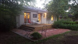 A house with a wooden deck, a dining area with a table and chairs, and a small garden with a bench. - Dallas Love Field Bluffview Bluebonnet Road Bungalow (Dallas)