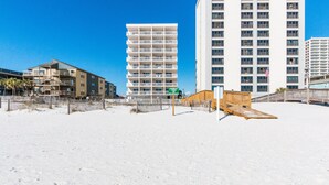 A beachfront hotel with multiple floors, a sandy beach in front, and a wooden boardwalk.