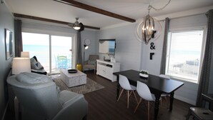A modern living room with a dining area, large windows, and a view of the ocean.