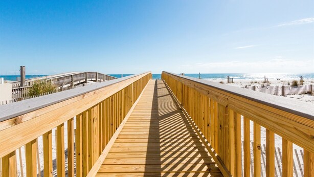 A wooden boardwalk leading to a beach with a clear sky.