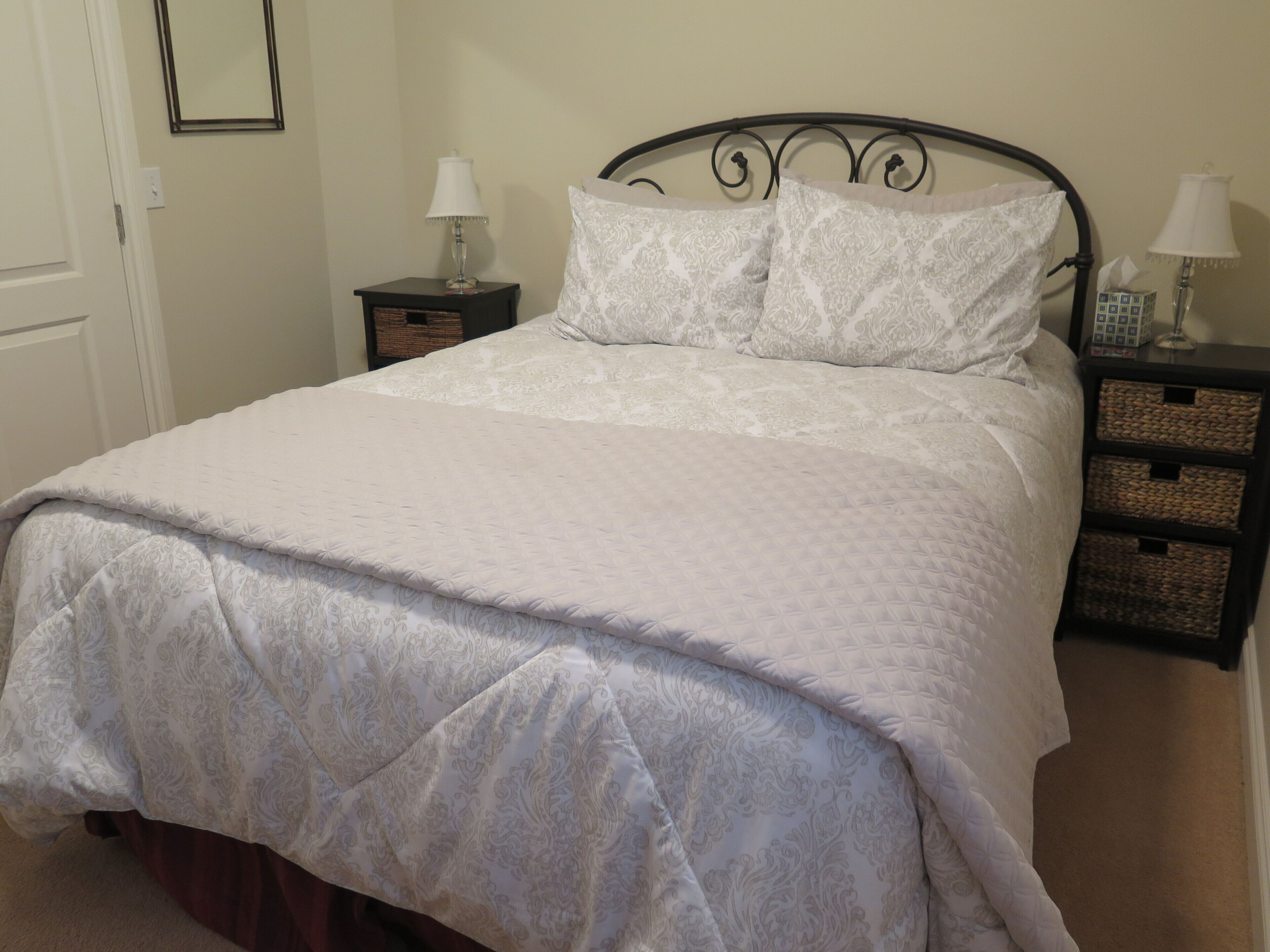 A neatly made bed with a patterned bedspread and pillows, flanked by two bedside tables with lamps and storage baskets.