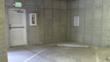 A parking garage with a concrete floor, marked parking space 103, an exit door, and a fire extinguisher.