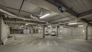 Eine mehrstöckige Parkgarage mit Betonpfeilern, Neonbeleuchtung und einigen parkenden Autos.