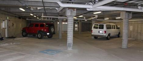 Un aparcamiento con dos vehículos estacionados, pilares de hormigón y tuberías aéreas.