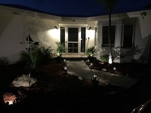Pathway leads to a modern entrance with glass panels and potted plants.