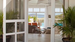 Ein sonnendurchflutetes Zimmer mit Blick auf einen Pool und Berge, ausgestattet mit einer Couch, einem Tisch und mehreren Kübelpflanzen.