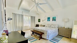 Ein Schlafzimmer mit einem Bett, Nachttischen, einem Schreibtisch, einem Stuhl, einem Deckenventilator und einem Fenster mit Vorhängen.