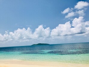 Una playa con agua turquesa cristalina, una orilla arenosa y una isla distante.