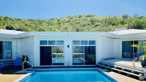 Ein Poolbereich mit freiem Blick auf den Pool, einer Sonnenterrasse und einer Hügelkulisse im Hintergrund.
