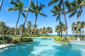 Piscina de resort com palmeiras e céu azul límpido.