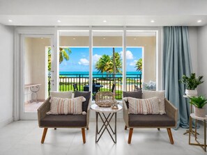 A room with two sofas facing a large window overlooking a beach and pool.