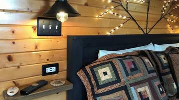 Ein gemütliches Zimmer mit einer Holzwand, einem Bett mit Steppdecke, einer Lampe und einer Wandsteckdose.