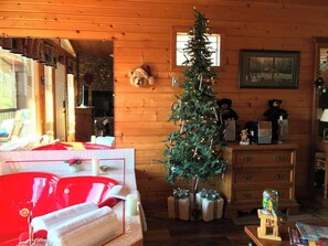 A cozy room with a wooden interior, a small Christmas tree, a red sofa, a dresser, and a teddy bear decoration.