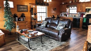 A cozy cabin interior with a leather sofa, wooden floors, a dining table, and a Christmas tree. - Honeymoon spot. Romantic. Great views. Private (Gatlinburg)