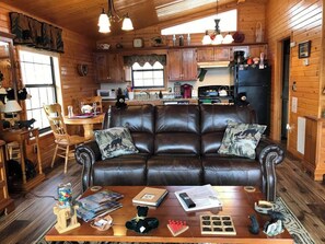 A cozy cabin interior with a leather sofa, wooden dining table, and a kitchen area.