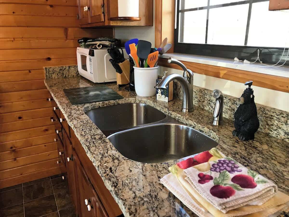 A kitchen with granite countertops, a double sink, wooden cabinets, and a window with blinds.