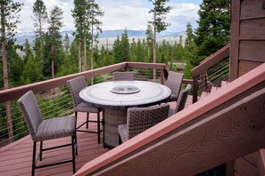En terrasse med et rundt bord og fletstole, med udsigt over et bjerglandskab.