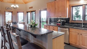 A modern kitchen with wooden cabinets, granite countertops, and a central island with seating. - Epic Views! Luxe Cabin near RMNP, Trails & Fishing, and #1 Ski Resort in US (Tabernash)