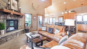 A spacious living room with a stone fireplace, leather sofas, and a large window. - Epic Views! Luxe Cabin near RMNP, Trails & Fishing, and #1 Ski Resort in US (Tabernash)