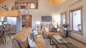 A spacious living room with a large brown leather sofa, a wooden coffee table, and a dining area with a kitchen in the background. - Epic Views! Luxe Cabin near RMNP, Trails & Fishing, and #1 Ski Resort in US (Tabernash)