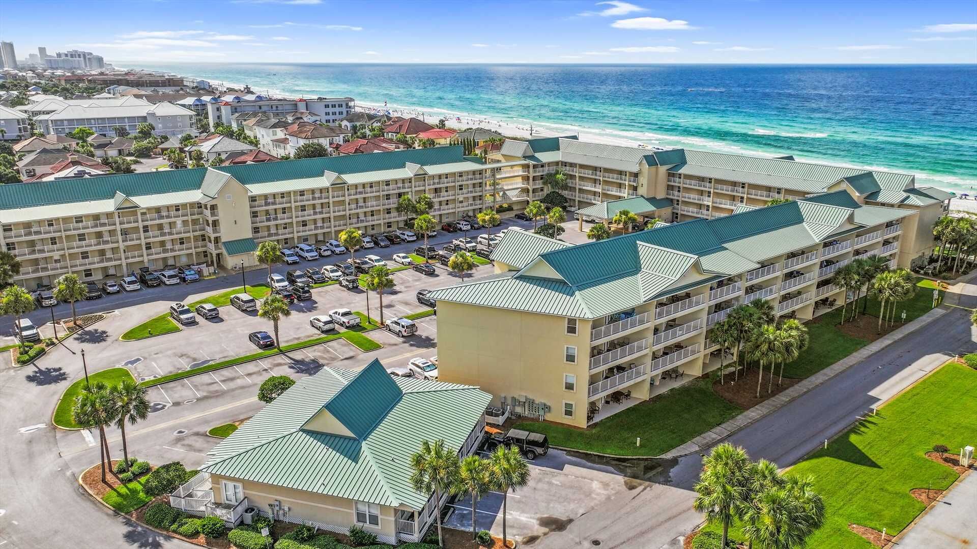 A hotel with multiple buildings, a parking lot, and a beach view.