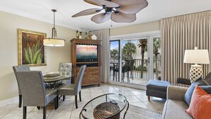 A living room with a dining area, a ceiling fan, a TV, and a view of the outdoors.
