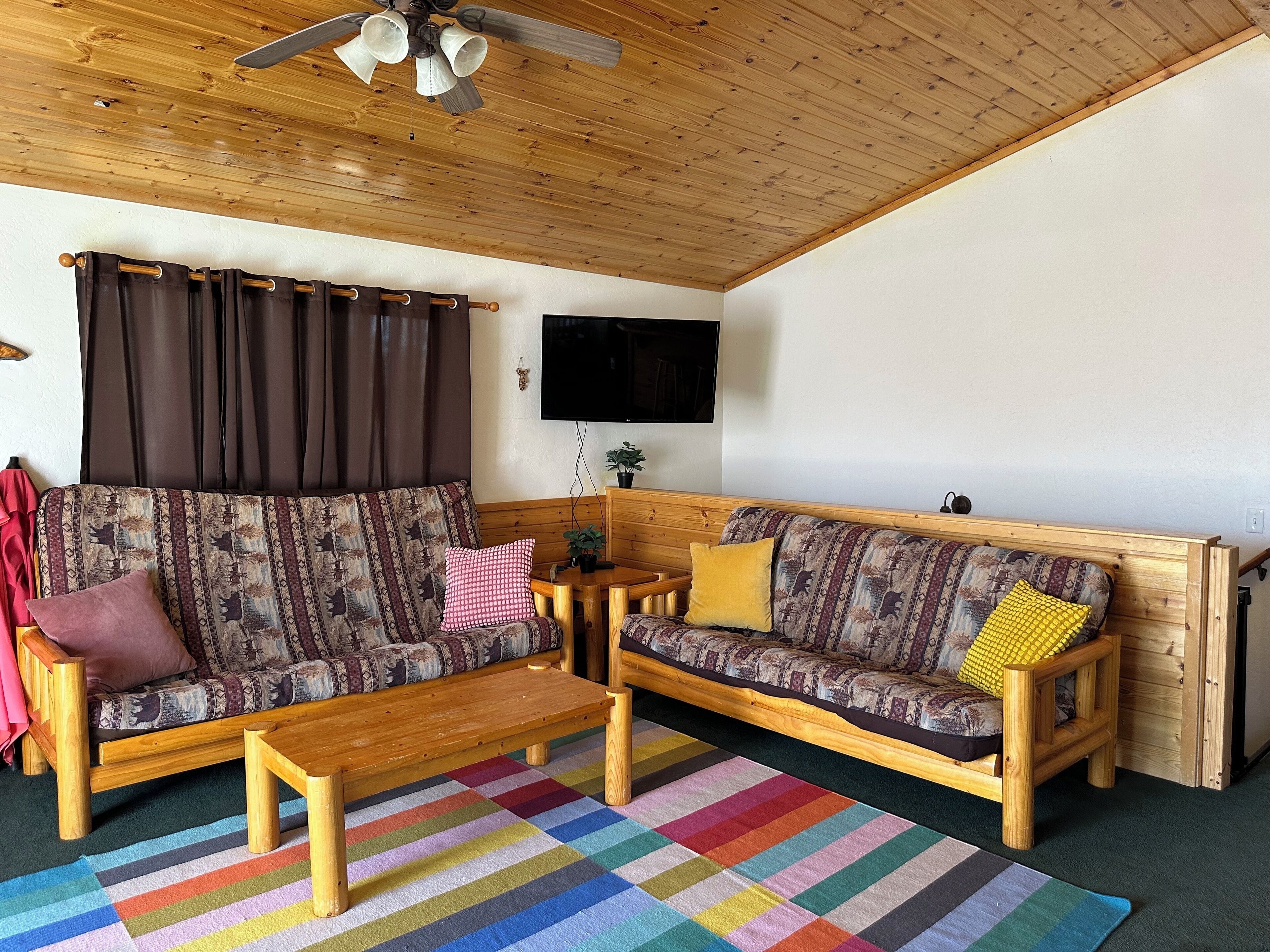 Un salon chaleureux avec deux canapés en bois, une table basse en bois et un tapis rayé aux couleurs vives.