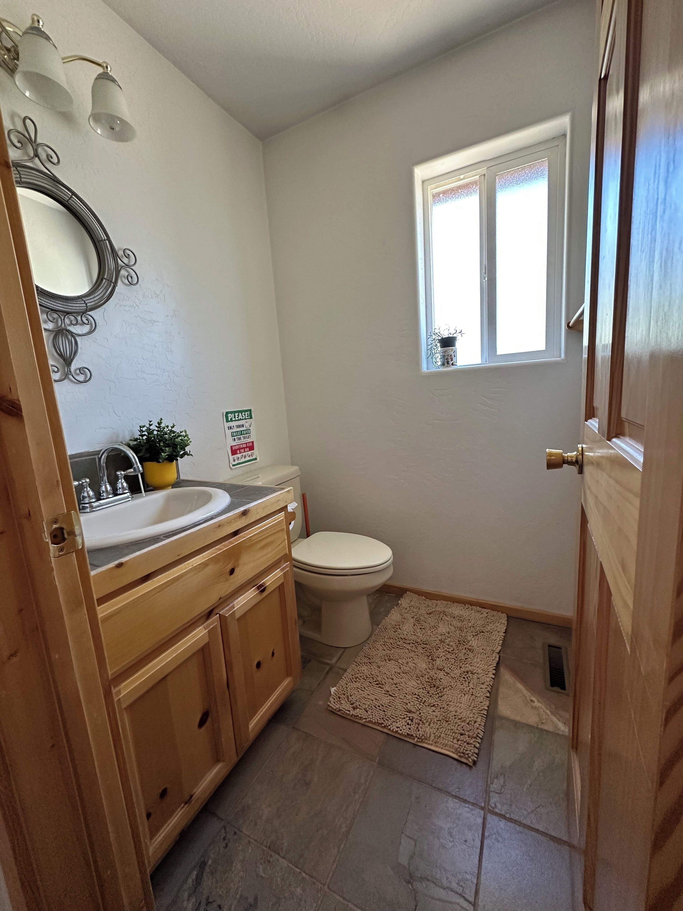 A bathroom with a sink, toilet, and a small window.