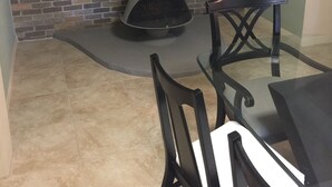 A room with a brick fireplace, a glass table, and black chairs.