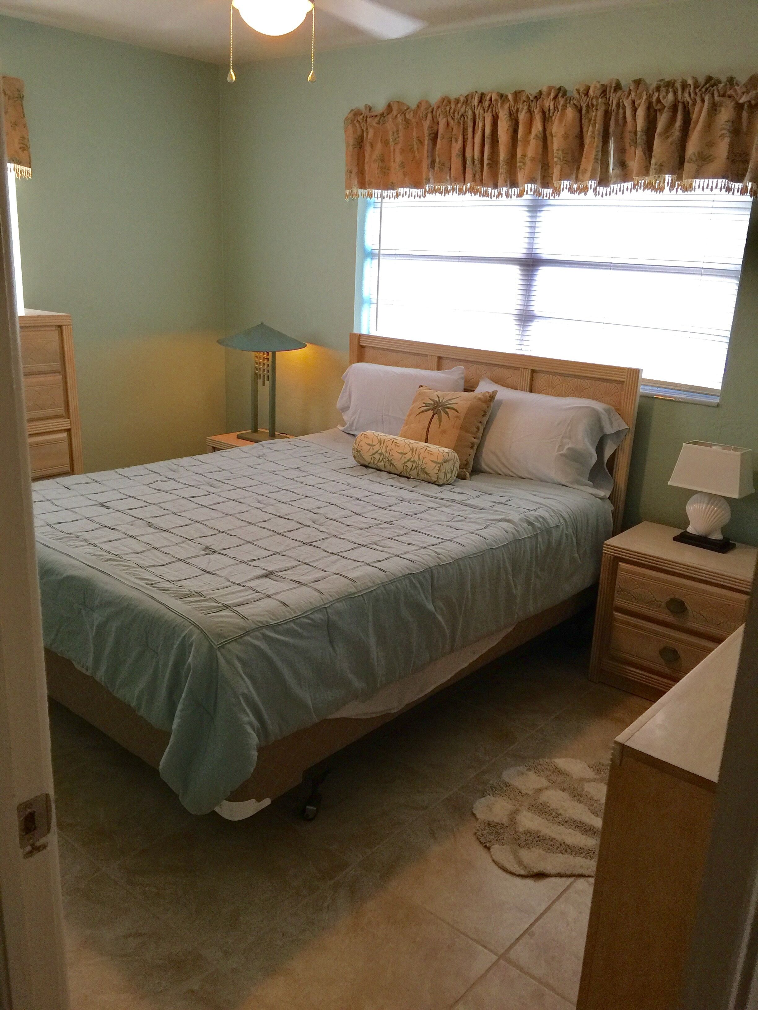 A bedroom with a bed, bedside tables, a lamp, a nightstand, and a window with curtains.