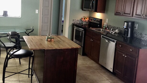 A kitchen with dark wooden cabinets, a central island with bar stools, a microwave, oven, and dishwasher.