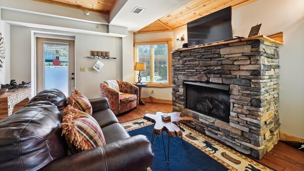A cozy living room with a stone fireplace, leather sofa, and a view of the outdoors through a window.