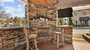 A stone fireplace with two wooden stools, a TV mounted on the wall, and a view of the street outside.