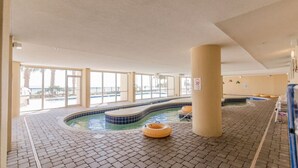 Une piscine intérieure avec un revêtement de sol carrelé, un jacuzzi et une grande colonne.