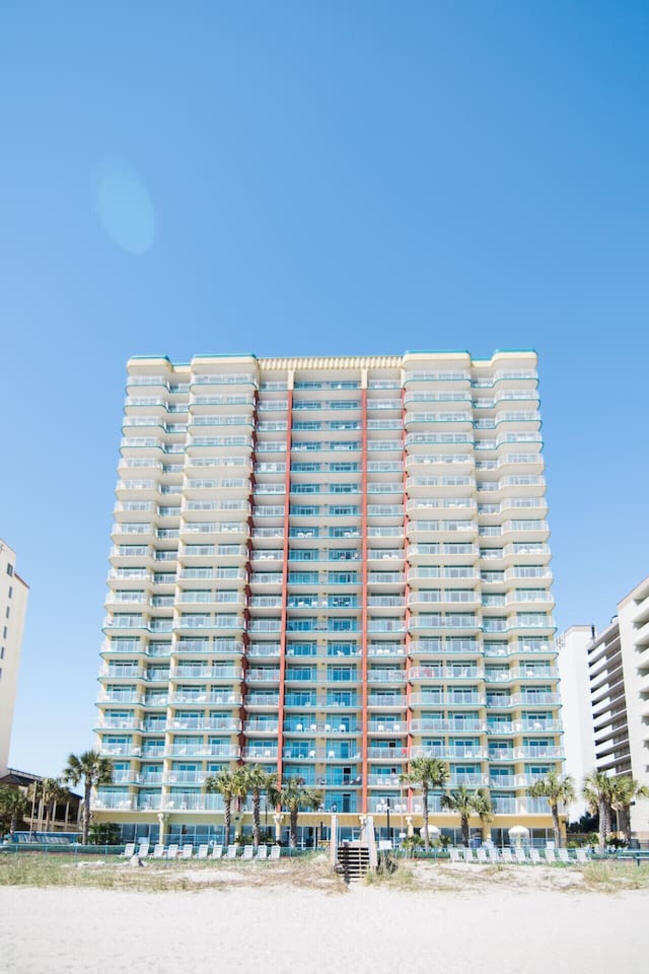 A high-rise hotel with multiple balconies, a beachside location, and a clear blue sky.
