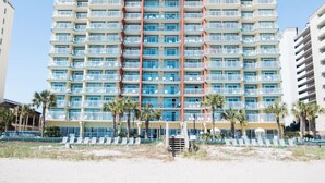 Un hôtel de grande hauteur doté de nombreux balcons, situé en bord de mer, avec un ciel bleu dégagé.